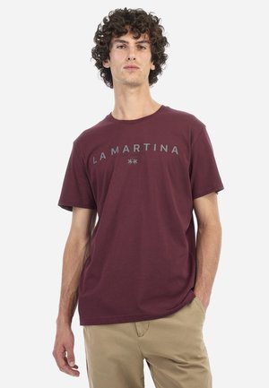T-shirt en coton bordeaux à manches courtes, col rond, avec le logo "LA MARTINA" en gris sur la poitrine. Coupe décontractée.