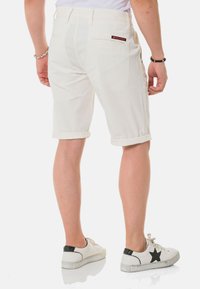 Shorts en jean blanc avec des ourlets repliés, deux poches arrière et une petite étiquette de logo. Portés avec des baskets blanches à accents verts.