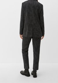 Completo grigio scuro su misura con tessuto testurizzato, caratterizzato da un motivo sottile. Include un blazer con maniche lunghe e pantaloni slim-fit. Stivali neri alla caviglia.
