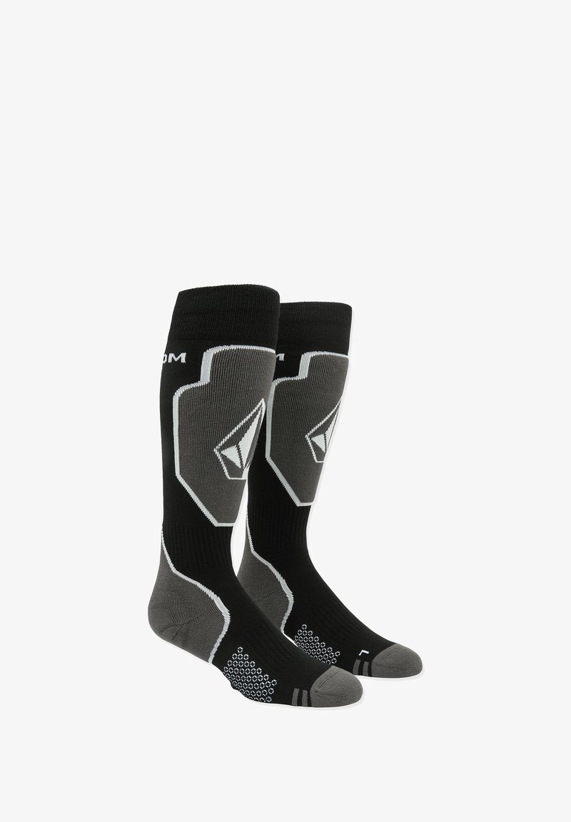 Chaussettes noires et grises à mi-mollet avec un grip hexagonal sur la semelle, présentant un design de logo argenté et des détails de piping contrastants.