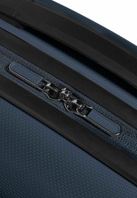 Donkerblauwe textuurtas met een robuuste rits en een metalen trekker, accentueert met vlakke zwarte rubberen rand en een merklabel.