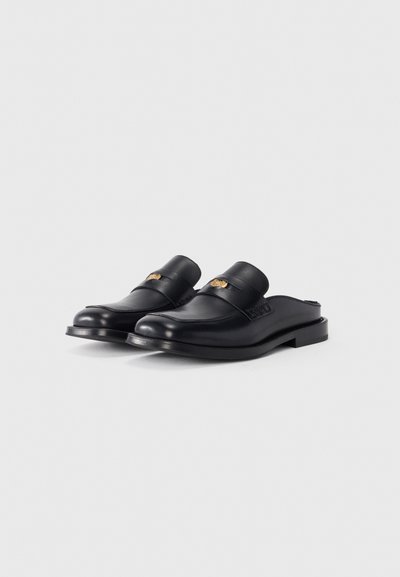 Sapatos pretos de couro, tipo slip-on, com um acabamento liso, bico arredondado e uma tira decorativa. Apresenta um discreto logotipo em relevo na parte da frente.