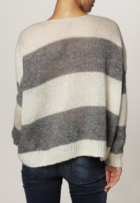 Stickad oversize tröja med breda grå och cremefärgade ränder, med lös passform och texturerat tyg. Rund halsringning och nedhasade axlar.