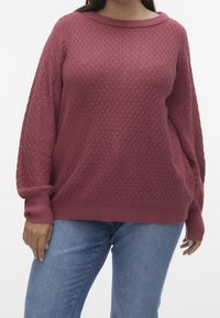 Un pull ample texturé de couleur rose profond avec un col rond et des poignets côtelés, associé à un jean en denim bleu clair.