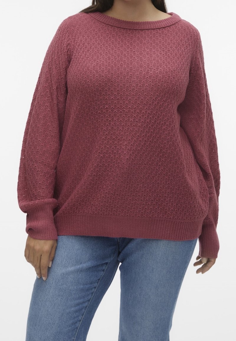 Un pull ample texturé de couleur rose profond avec un col rond et des poignets côtelés, associé à un jean en denim bleu clair.