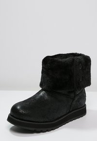 Czarne botki na kostkę z futra sztucznego o teksturowanej, błyszczącej powierzchni z szerokim mankietem ozdobionym dwoma guzikami. Płaska podeszwa i zaokrąglony czubek.