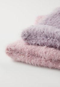 Drie zachte, fluffy textielen in gedempte roze en lavendel tinten netjes gestapeld, met een fuzzy, gestructureerd oppervlak.