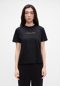 Čierne bavlnené tričko s okrúhlym výstrihom a krátkymi rukávmi. Na hrudi je potlačené zlaté logo "Calvin Klein". Hladká textúra.