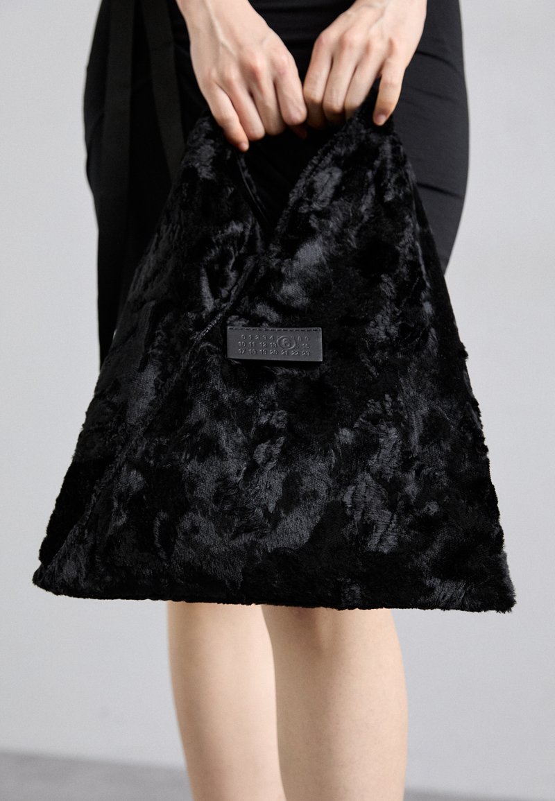 Bolsa de pele sintética preta com uma forma triangular e superfície texturizada, apresentando um pequeno rótulo retangular de um lado.