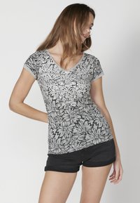 Tricou gri cu flori, cu decolteu în formă de V și mâneci scurte, având un model floral texturat în negru și argintiu. Asortat cu șorturi negre.