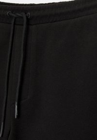 Schwarze Baumwoll-Jogginghosen mit strukturierter Oberfläche, verstellbarem Zugbandbund und einem dezenten Markenlabel an der Seite.