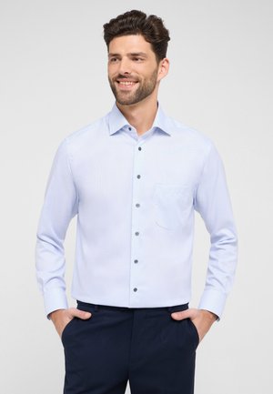Hellblaue Langarmbluse mit einer Knopfleiste, einer Brusttasche und dunklen Knöpfen. Strukturierter Stoff mit einem dezenten Muster.