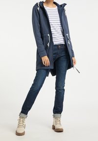 Navy hooded jacket with white drawstring details, paired with a striped shirt and dark blue jeans, complemented by light beige lace-up boots.