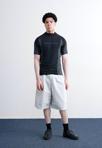 Camisola atlética preta de mangas curtas com um decote alto, combinada com calções brancos de corte largo, meias pretas e sapatilhas.
