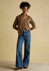 Pruun ja meresinine triibuline pika varrukaga topp, millel on särgikaelus, koos kõrge vöökohaga laia säärega siniste teksade ja pruunide lapikutega.