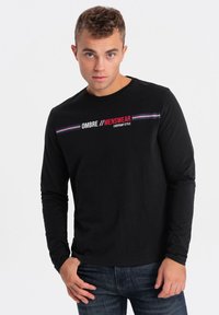 Schwarzes Langarm-T-Shirt aus Baumwolle mit dem bedruckten Text "OMBRE // MENSWEAR" in Rot und Weiß, versehen mit horizontalen Streifen in Blau und Rot.