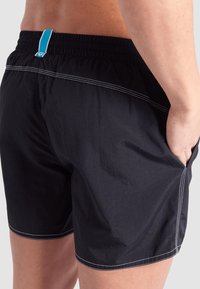 Pantaloni da nuoto neri realizzati in tessuto leggero, con cuciture bianche e un'asola blu sul retro, dotati di tasche laterali.