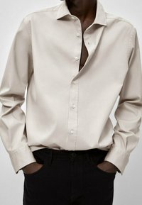 Beżowa koszula na guziki z gładkiego materiału, z klasycznym kołnierzem i długimi rękawami. Stylizowana z czarnymi spodniami o luźnym kroju.