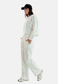 Witte cropped sweatshirt gecombineerd met bijpassende hoog-waistbroek, met zijsstripes en een elastische tailleband. Getextureerde stof, casual ontwerp.