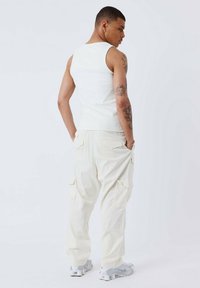 Top in cotone bianco con un design aderente, abbinato a pantaloni cargo beige chiaro con più tasche. Il modello indossa sneakers grigie.