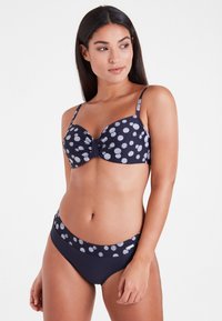 Marineblaues Bikini-Set mit weißem Punktmuster. Das Unterwäscheoberteil mit Bügel verfügt über eine geknotete Detail, verstellbare Träger. Hochgeschnittene Unterteile bieten guten Halt.