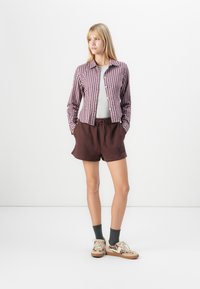 Rutet knap-op skjorte i bordeaux og hvid, grå t-shirt underneath, brune shorts med broderet logo og mønstrede sneakers.