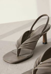 Gray leather heeled sandals with a twisted design at the toe, slender ankle strap, and a square heel. Smooth texture and minimalist style.