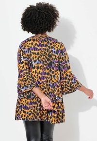 Langsleeve tuniek in een levendig oranje, paarse en zwarte dierenprint; beschikt over een losse pasvorm en een gelaagd ontwerp. Gemaakt van lichte stof.