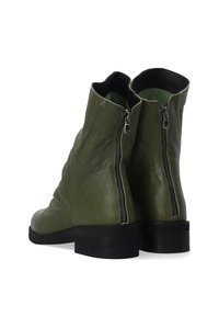 Grüne Leder Stiefeletten mit schlaffem Design, ausgestattet mit zwei seitlichen Reißverschlüssen und einem schwarzen flachen Absatz. Glatte Textur mit matter Oberfläche.