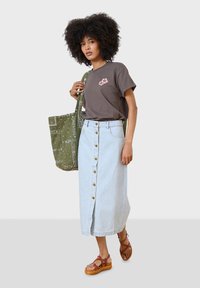 Camiseta de algodón marrón con bordado floral rosa, falda midi de botones frontales de mezclilla azul claro, bolso de mano verde con estampado, sandalias marrones con tiras.