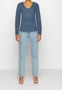 Blå stickad tröja med v-ringning och långa ärmar, kombinerad med ljusa raka jeans och vita klackskalor med remmar.