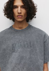 Grå oversized t-shirt med en falmet "NIRVANA" tryk. Lavet af blød bomuld, med rund halsudskæring og korte ærmer. Tekstureret vaskeeffekt.