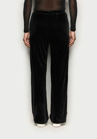Černé sametové kalhoty s volným střihem a elastickým pasem, s hladkou texturou a širokými nohavicemi. Minimalistický design bez dalších akcentů.