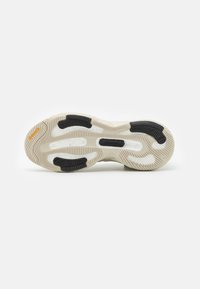 Sula av beigefärgad och svart sneakers med texturerat grepp, Boost-dämpning, Adidas-logotyp och orange Continental-märkesprofil på en vit bakgrund.