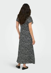 Maxi-jurk van zwarte stof met een klein wit bloemenpatroon. Korte zwierige mouwen, aansluitend lijfje en vloeiende rok. Draagt het met zwarte ballerina's.
