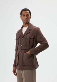 Braune, strukturierte Jacke mit tailliertem Gürtel, vier Fronttaschen und Knopfverschluss. Verfügt über einen traditionellen Kragen und lange Ärmel.