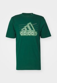 Camiseta de algodón verde con logo de adidas en blanco con diseño de contorno. Manga corta, cuello redondo y un corte holgado.