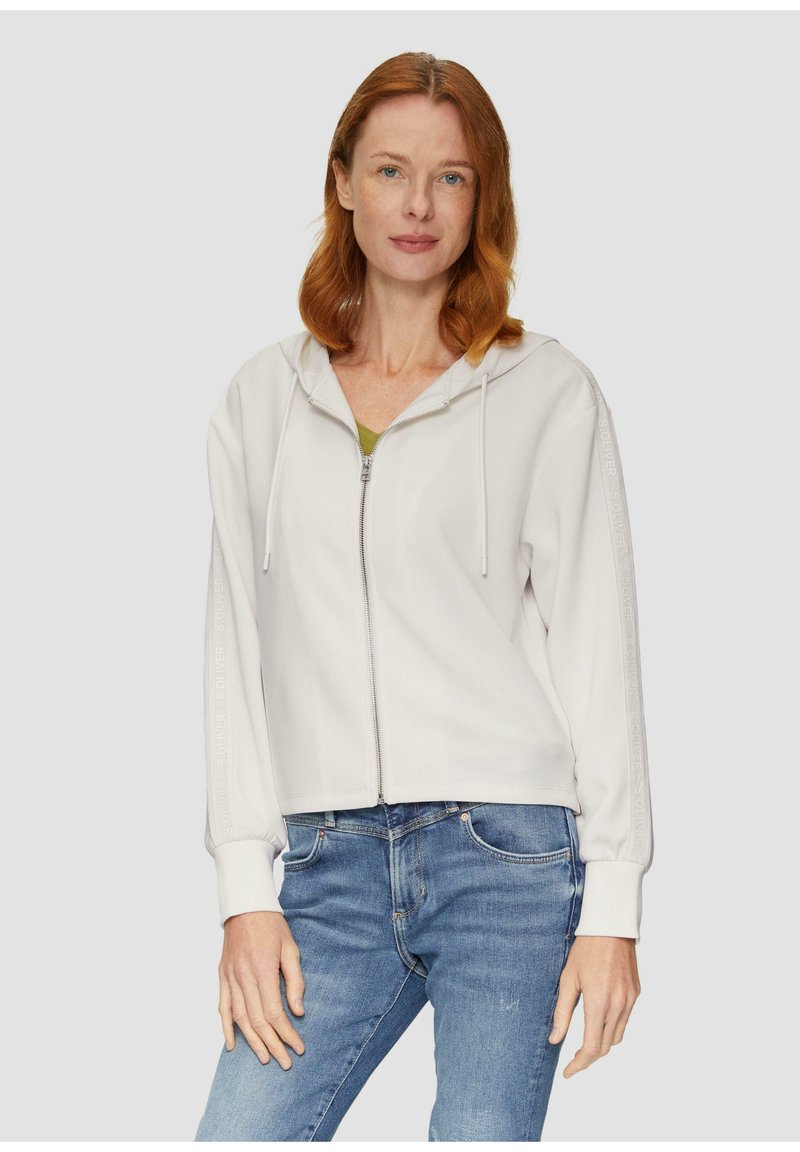 Lichtgrijze zip-up hoodie met een capuchon en koordjes, voorzien van gestructureerde zijstrepen en geribbelde manchetten, gecombineerd met denim jeans.