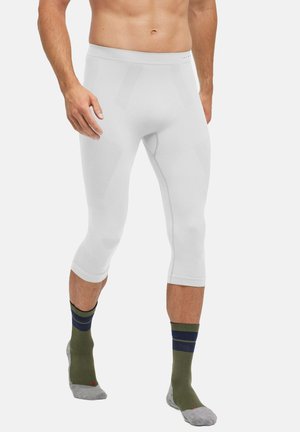 Leggings compressivi bianchi da uomo con design aderente e pannelli testurizzati. Indossati con calze a righe verdi e grigie.