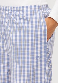 Blå och vit rutiga byxor med elastisk midja och fickor. Har broderad logotyp på vänster sida. Tyget är lätt och lent.