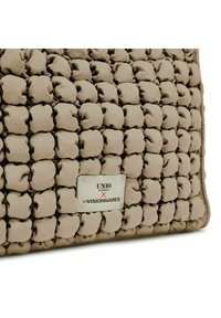 Sac matelassé beige avec une surface texturée en forme de bulles. Comprend une plaque logo métallique avec l'inscription "UNIO x LES VISIONNAIRES."