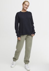 Pull en maille texturée bleu marine avec un col rond, associé à un pantalon de jogging tapered vert olive clair et des baskets blanches.