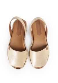 Kultaiset metallinhohtoiset liukupalakengät, joissa on luonnollinen nahkasisus ja juuttireunus. Avoin varvas- ja kantapäämuotoilu, jossa on sileä rakenne.