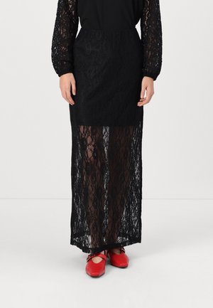 Sort lang nederdel i blonder med gennemsigtig underdel, båret med røde Mary Jane-flade sko og sort top med blonderærmer.