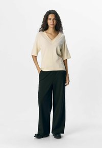 Beżowy sweter z dekoltem w serek i krótkim rękawem, w połączeniu z luźnymi czarnymi spodniami i masywnymi czarnymi butami. Prosty design o miękkiej fakturze.