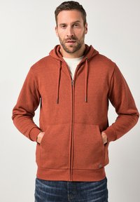 Rustfarbenes Zip-Up-Hoodie mit Kängurutasche, Kapuze mit Kordelzug und gerippten Bündchen. Hergestellt aus weichem Stoff mit einer strukturierten Oberfläche.