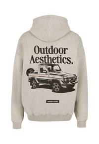Felpa beige con grafica nera di un veicolo fuoristrada e testo "Outdoor Aesthetics" e "Another Cotton" sul retro.