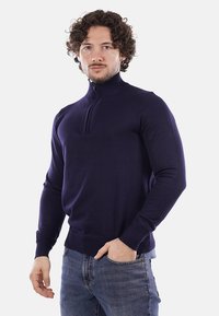 Maglione zip con colletto alto di colore blu navy, realizzato in un morbido tessuto a maglia, con maniche a costine e una silhouette aderente.