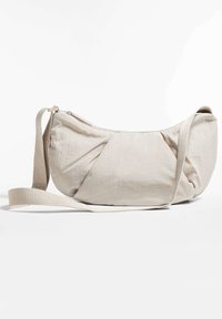 Bezs színű textil táska gyűrt részletekkel, cipzáros záródással és hosszú, állíthat�ó pánttal. Simább textúra és ívelt, lekerekített forma.