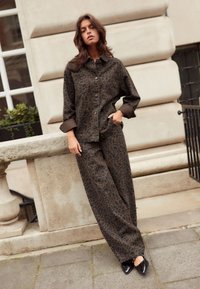 Veste à imprimé léopard marron et pantalon large en tissu doux, avec des accents noirs et des boutons, associés à des ballerines noires à bout pointu.